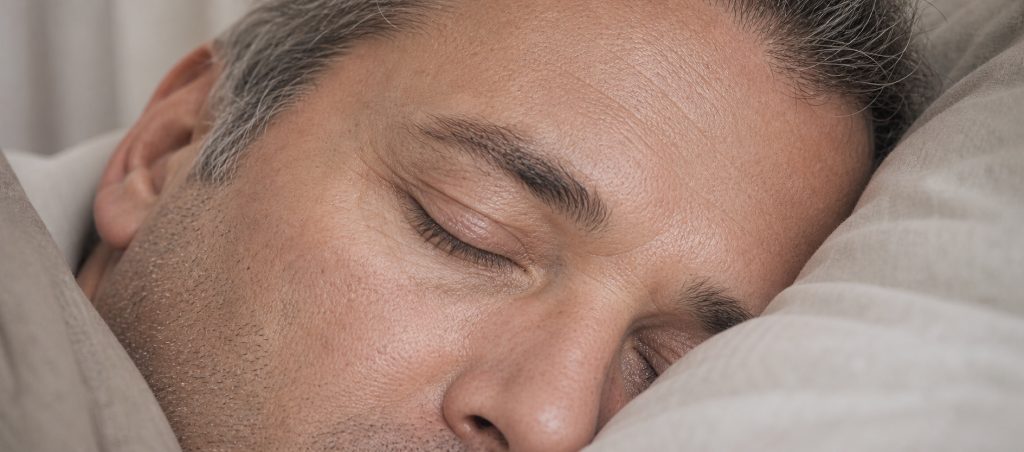 Photographie rapprochée d’un homme dormant sur le côté, la paupière fermée contre l’oreiller